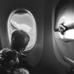 Black and white photo of boy looking out window of airplane