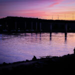 COlor photo of sunset and silhouetted fishermen below the Big Dam Bridge on the Arkansas River near Little Rock
