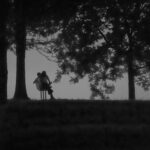 Black and white photo of couple in silhouette on a park bench at sunset on Arkansas River.