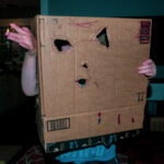 color photo of boy in a robot costume he made from an amazon prime shipping box