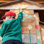 color photograph of boy reaching to open chicken henhouse coop door to collect eggs