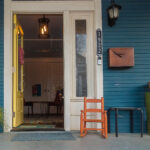color photograph of an orange baby rocking chair on a blue front porch with a yellow open front door in little rock arkansas